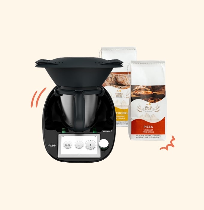 Ein schwarzer Küchenmaschine mit einem rechten Griff und einem digitalen Bedienfeld steht im Vordergrund. Im Hintergrund befinden sich zwei Säcke mit Mehl für Brot und Pizza. Die Maschinen und Zutaten bieten eine Grundlage für vielfältige Kochmöglichkeiten.