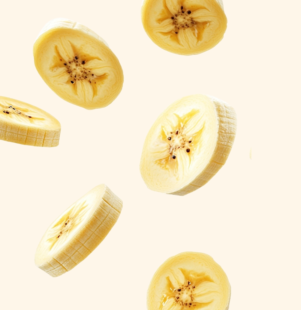 Sliced bananas schweben vor einem neutralen, hellen Hintergrund. Die Schnitte zeigen die charakteristische gelbe Farbe und die feine Struktur des Fruchtfleisches. Die Anordnung der Scheiben vermittelt eine dynamische und frische Atmosphäre.