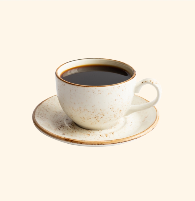Eine weiße Kaffeetasse mit schwarzem Kaffee steht auf einem kleinen, passenden Unterteller. Die Tasse hat eine rustikale Optik mit kleinen Punkten und einem leicht abgenutzten Rand. Der Hintergrund ist neutral und hell.