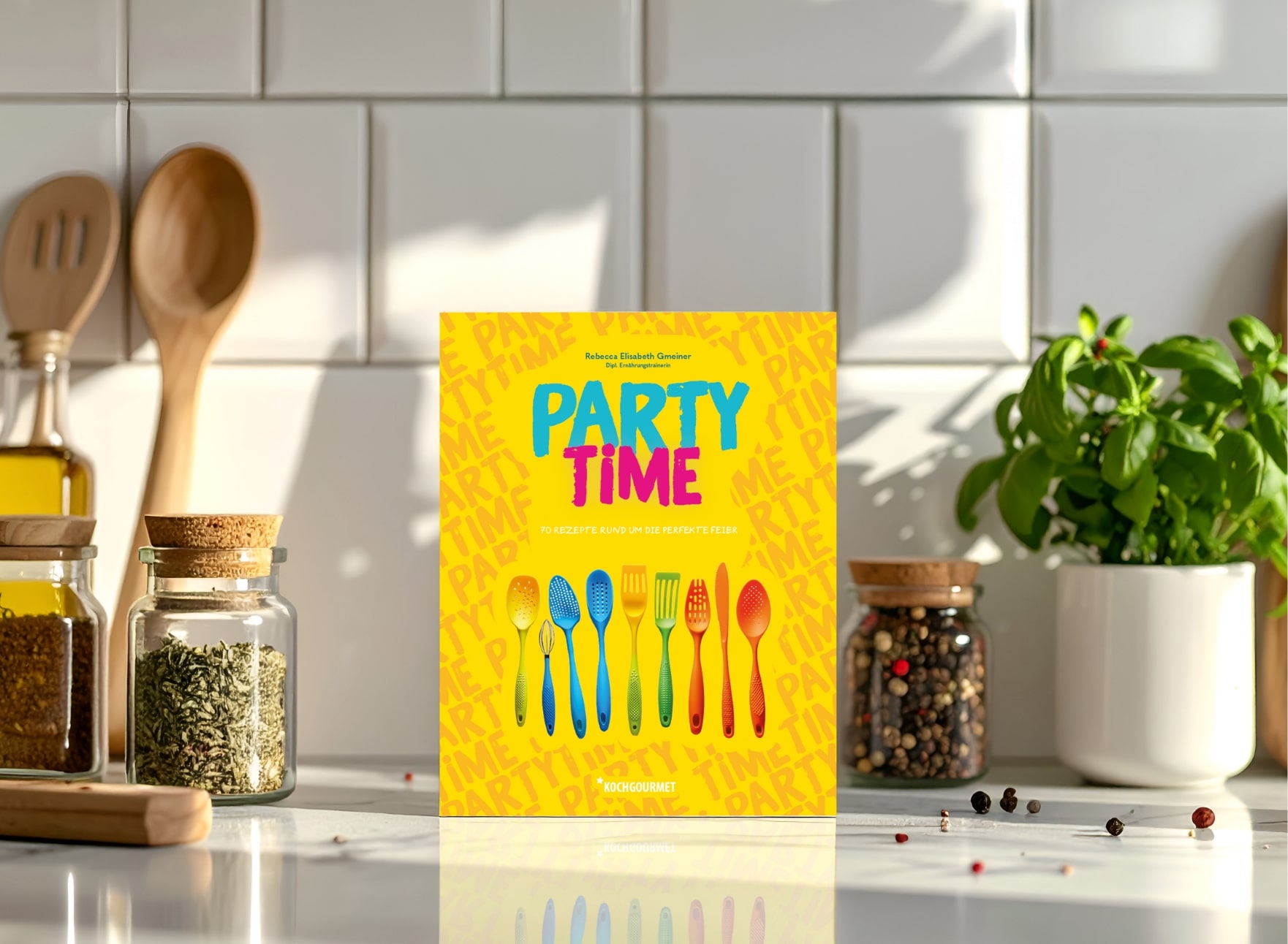Auf dem Bild ist ein Kochbuch mit dem Titel "PARTY TIME" auf einem Tisch zu sehen. Es enthält bunte Abbildungen von Besteck und bietet 70 Rezepte für Feiern. Im Hintergrund sind Kräuter und Gewürze in Gläsern sowie Küchenutensilien sichtbar.