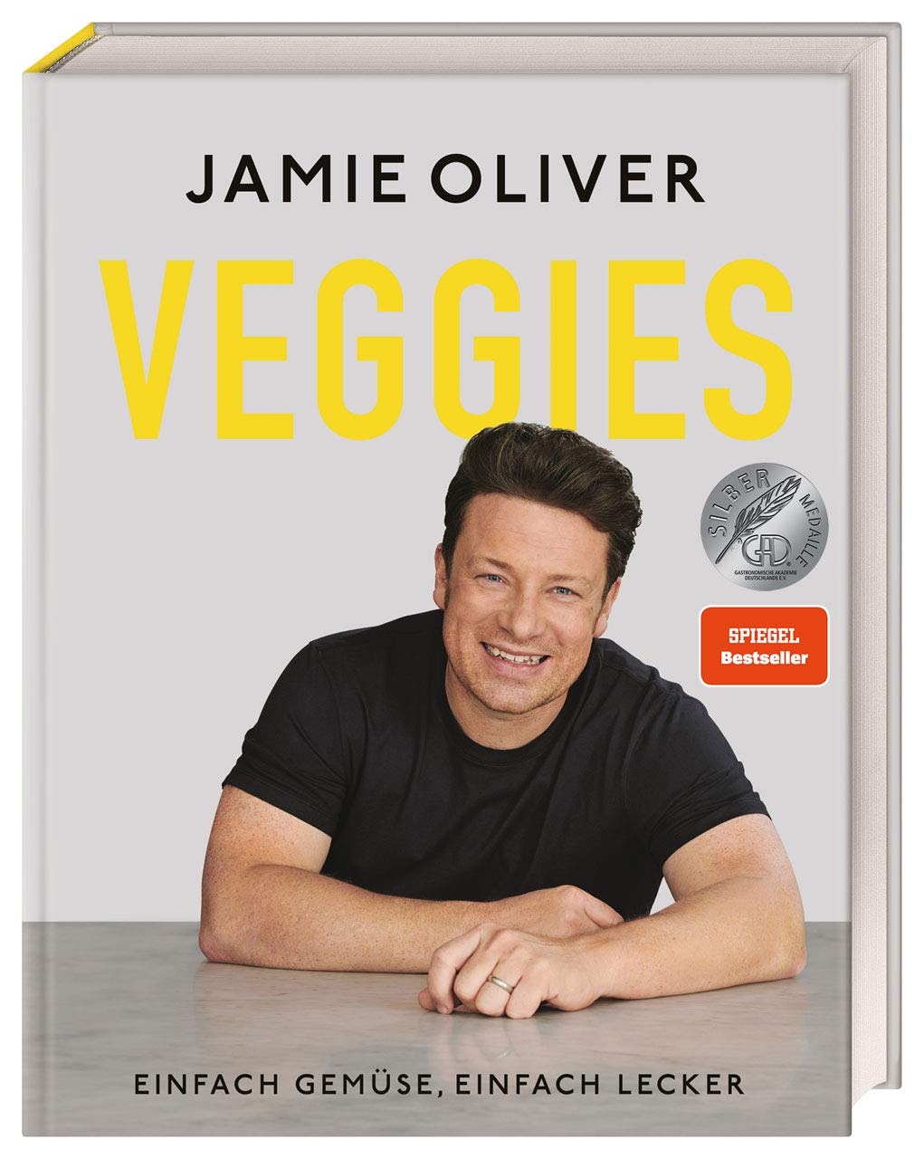 Ein Kochbuch von Jamie Oliver mit dem Titel "Veggies". Das Cover zeigt den Autor lächelnd mit schwarzem T-Shirt. Darunter steht der Untertitel "Einfach Gemüse, einfach lecker". Es sind auch Auszeichnungen und Hinweise auf Bestseller enthalten.