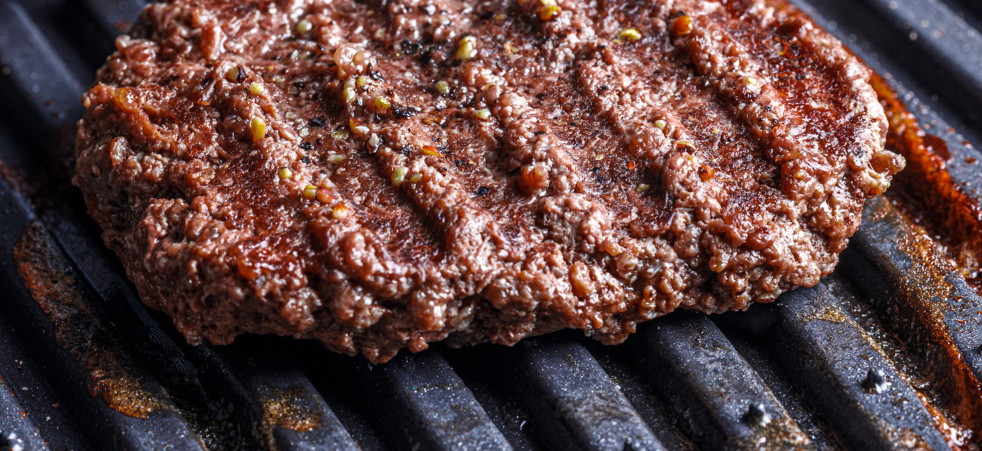 Ein gegrilltes Rindersteak liegt auf einem Grillrost. Die Oberfläche ist gut gebräunt mit grilltypischen Streifen, und es sind einige Gewürze sichtbar. Das Steak wirkt saftig und appetitlich.