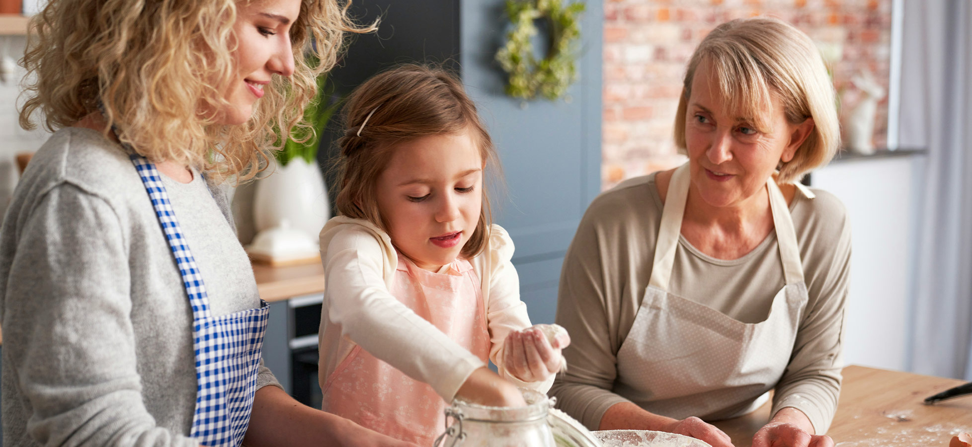 Drei Personen in einer Küche zusammen beim Backen. Ein Mädchen greift in ein Glas mit Mehl, während zwei Erwachsene aufmerksam zuschauen und lächeln. Die Atmosphäre ist freundlich und familiär, umgeben von Küchenutensilien.