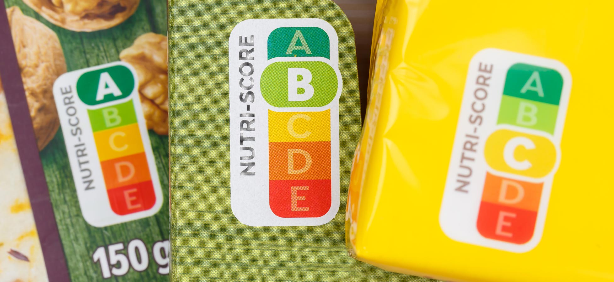 Auf dem Bild sind mehrere Nahrungsmittelverpackungen zu sehen, die den Nutri-Score zeigen. Dieser Score ist eine farbcodierte Kennzeichnung mit den Buchstaben A bis E, die die Nährwertqualität der Produkte bewertet. A steht für die beste und E für die schlechteste Bewertung.