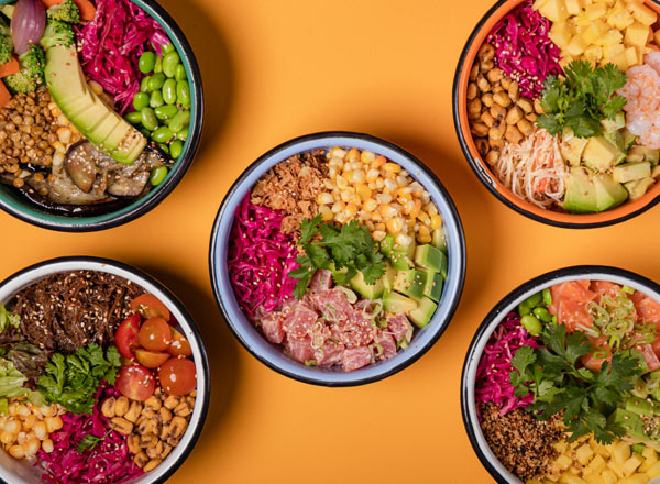 Fünf bunte Schalen mit verschiedenen Zutaten, darunter Gemüse, Obst, Tofu, Fisch und Kräuter, angeordnet auf einem orangefarbenen Hintergrund. Jede Schale bietet eine vielfältige Kombination, die Appetit anregt und gesund aussieht.
