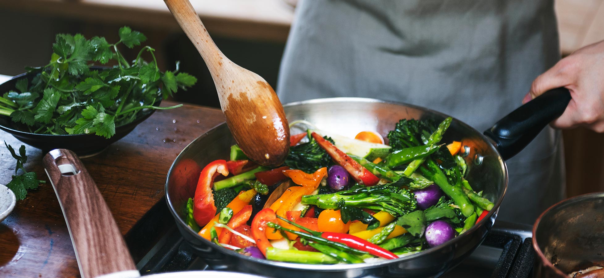 Zwei Männer sitzen an einem Tisch und halten große Stücke Pizza in den Händen. Der Mann links lächelt und knifft ein Auge zu, während der Mann rechts ernst schaut. Beide genießen ihre Pizza und haben Getränke vor sich.