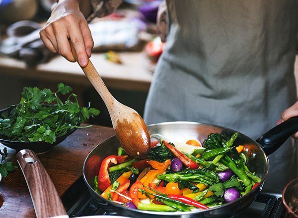 Zwei Männer sitzen an einem Tisch und halten jeweils ein Stück Pizza in den Händen. Der Mann links hat eine Pizza mit viel Belag, während der Mann rechts ein Stück mit Rucola präsentiert. Auf dem Tisch stehen zwei Getränke in durchsichtigen Bechern.