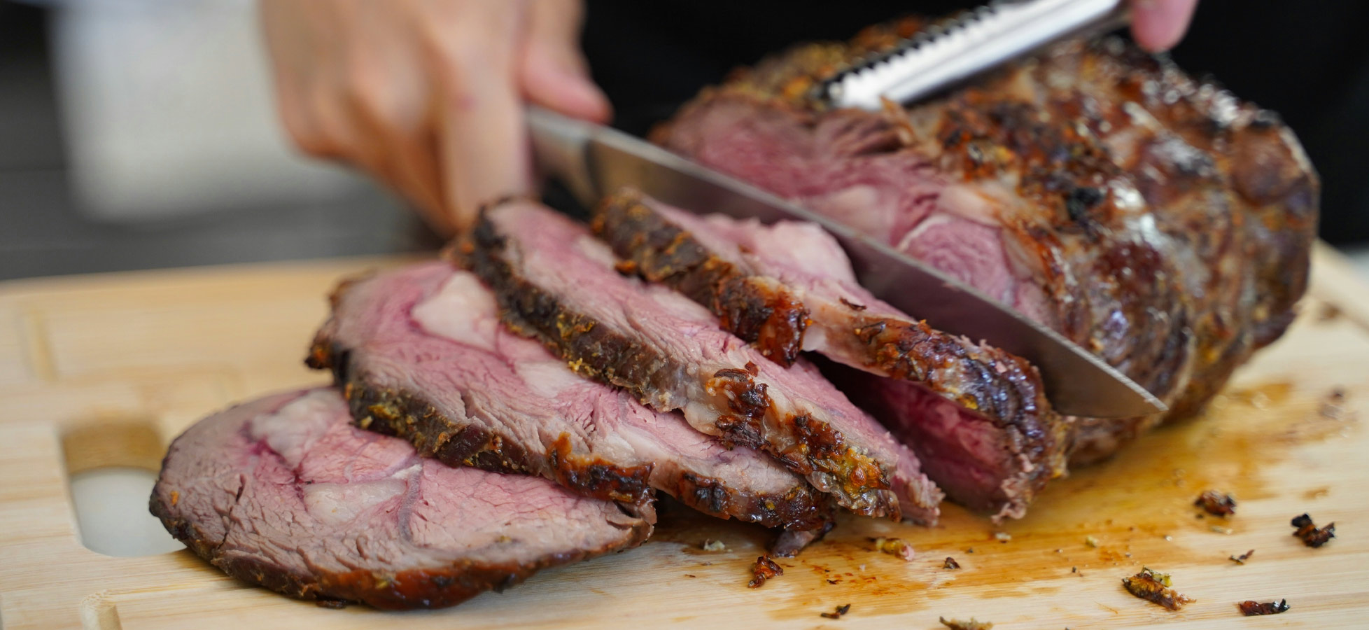 Ein frisch geschnittenes Bratenstück liegt auf einem Holzbrett. An einem Teil des Bratens sind mehrere gleichmäßige, saftige Scheiben abgeschnitten. Die Oberfläche ist knusprig und goldbraun, während das Fleisch innen rosa und zart erscheint. Ein fleischiges Gericht, das zum Servieren fertig ist.