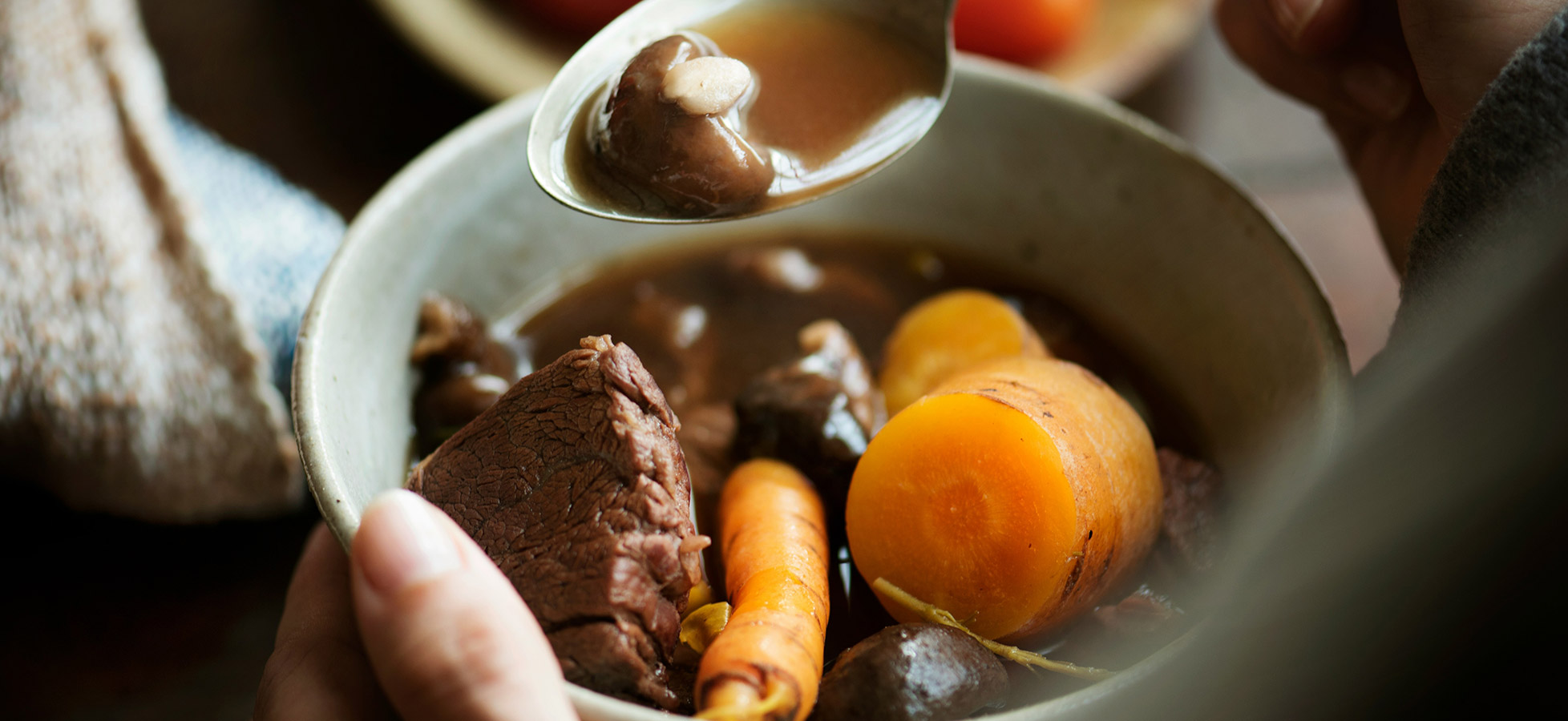 Eine lächelnde Frau sitzt an einem Tisch, vor ihr stehen zwei Schalen mit Essen: eine Schale mit Reis und eine mit einer würzigen Sauce sowie frittierten Bällchen. Sie scheint das Essen zu genießen und hat die Hände auf den Tisch gelegt.