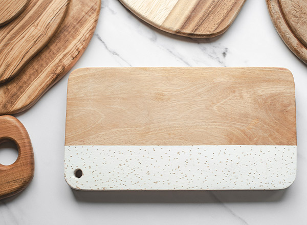 Eine Holzschneidebrett mit einer weißen, marmorierten Kante und einem Loch zur Aufhängung, umgeben von weiteren Holzbrettchen in unterschiedlichen Formen. Die Oberfläche des Bretts ist glatt und nahezu leer.