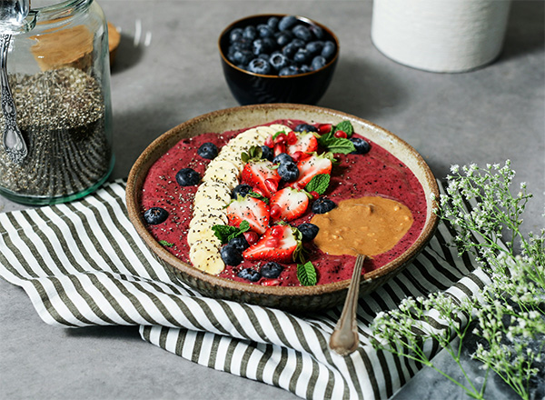 Eine Smoothie-Schüssel, garniert mit Bananenscheiben, Erdbeeren, Blaubeeren, Chiasamen, Minzblättern und Erdnussbutter.
