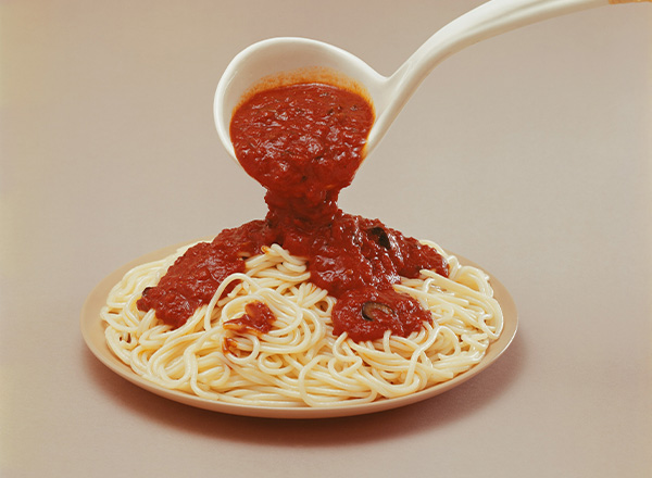 Ein Teller Spaghetti wird mit einer großzügigen Portion Tomatensauce übergossen. Die Spaghetti sind weich und in einer kreisförmigen Anordnung auf dem Teller. Die Sauce ist dick und hat eine tiefrote Farbe.