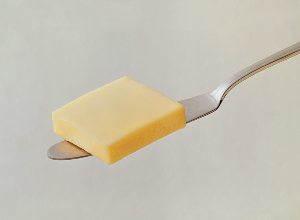 Ein Stück gelbe Butter liegt auf einem Löffel. Der Löffel ist aus Silber und hebt das Stück Butter leicht an. Der Hintergrund ist neutral und unauffällig, um die Aufmerksamkeit auf die Butter zu lenken.