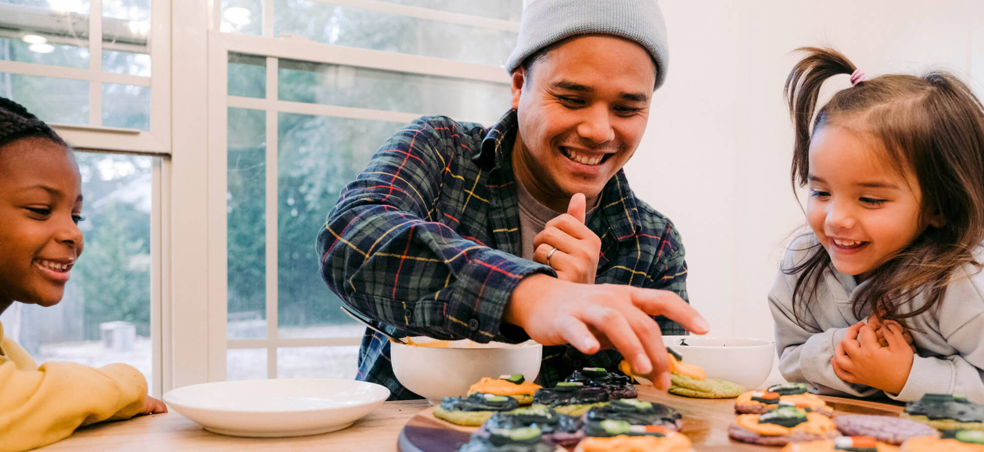 Eine Hand streut Mehl auf eine glatte Fläche. In der Nähe liegen eine Rührschüssel mit Mehl, ein Schneebesen, ein Wasserbehälter und ein Esslöffel Salz. Die Umgebung ist hell und hat sanfte Farbtöne, die eine gemütliche Backatmosphäre schaffen.