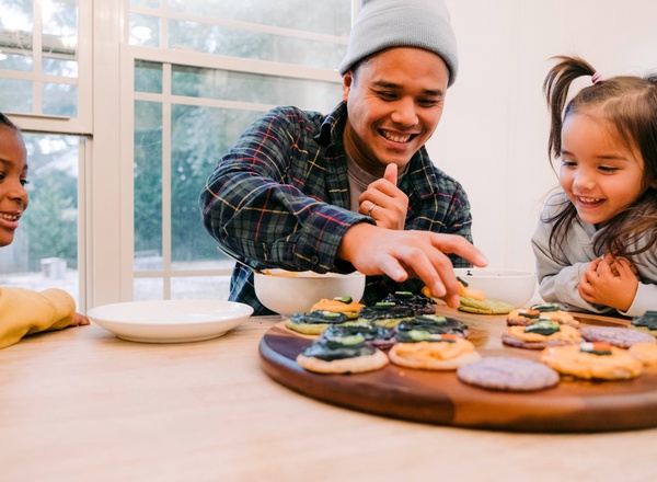 Hände formen Teig aus Mehl auf einer Arbeitsfläche. Neben den Händen liegen eine Schüssel mit Mehl, eine Schüssel mit Wasser, ein Schneebesen, ein Messlöffel und ein Pinsel. Es ist Zutaten für das Backen zu sehen.