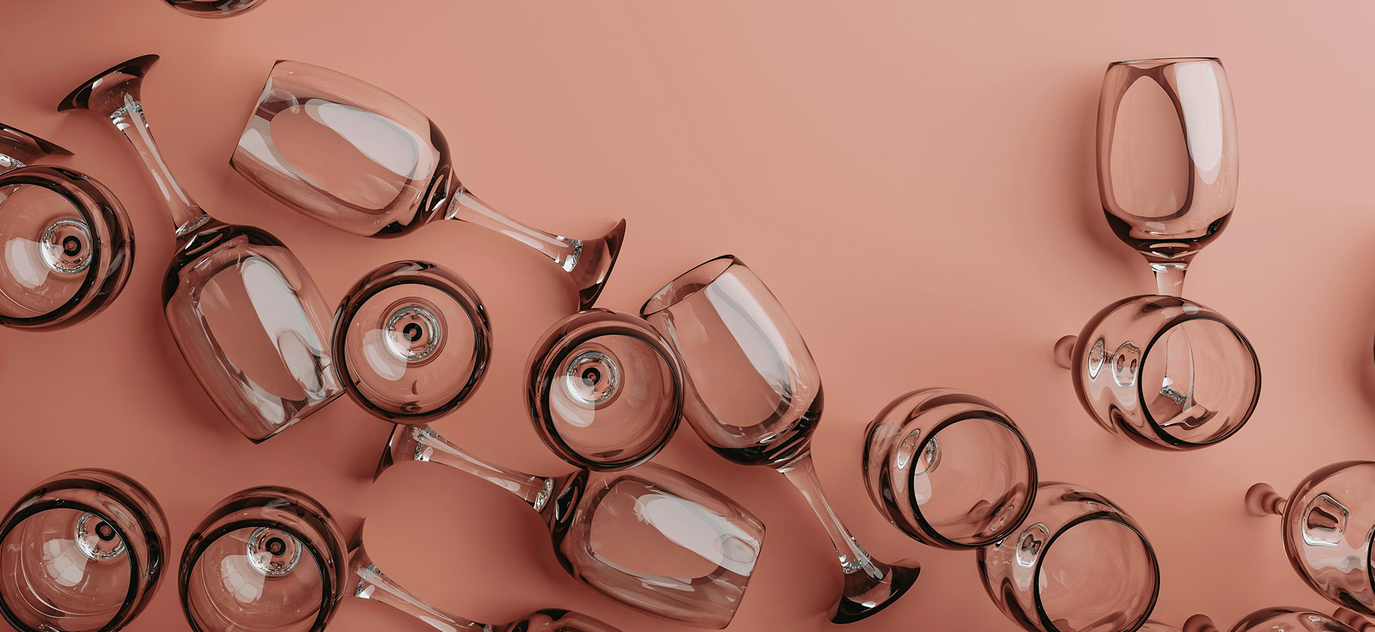 Eine Gruppe von Glasweingläsern liegt chaotisch auf einem rosa Hintergrund. Die Gläser variieren in Form und Position, einige stehen aufrecht, während andere umgedreht sind. Die glatte Oberfläche der Gläser reflektiert Licht und erzeugt einen glänzenden Effekt.
