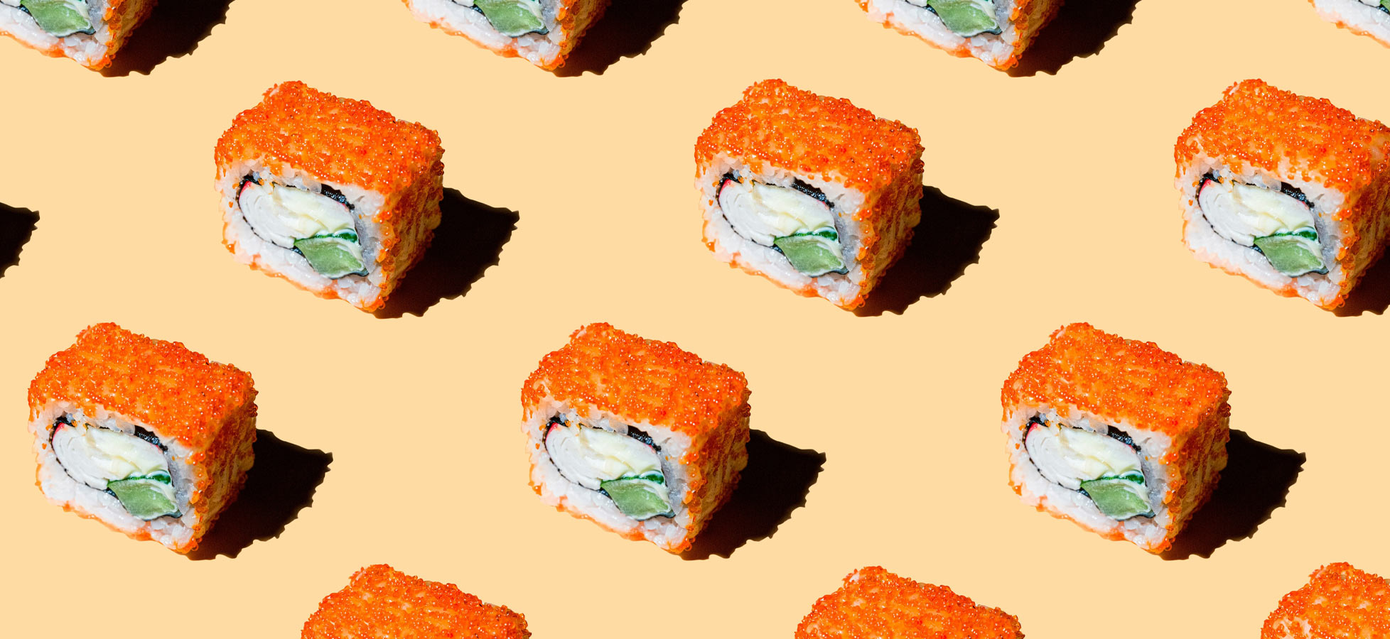 Eine wiederholte Anordnung von Sushi-Rollen auf einem orangefarbenen Hintergrund. Jede Rolle hat eine leuchtend orangefarbene Oberfläche aus Fischrogen und enthält Gurken- und Füllungen wie Avocado. Die Sushi-Teile haben eine rechteckige Form.
