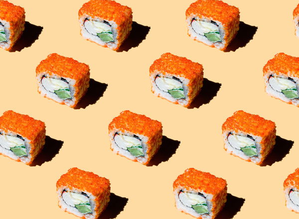 Muster von Sushi-Röllchen auf einem einfarbigen Hintergrund. Die Röllchen sind mit orangefarbenem Fischrogen umhüllt und enthalten gefüllte Zutaten, die sichtbar sind. Das Bild vermittelt eine appetitliche und ansprechende Präsentation von Sushi.