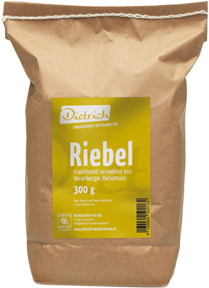 Packung mit Riebelmehl. Die braune Tüte trägt ein gelbes Etikett mit der Aufschrift "Riebel", sowie Informationen über das Produkt. Es handelt sich um 300 g traditionell vermahlenes Riebelmehl aus Vorarlberg. Hersteller ist Dietrich.