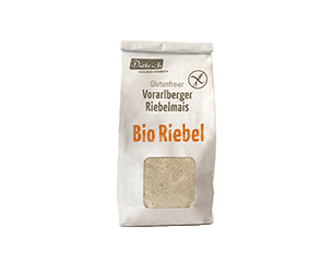 Papiertüte mit Bio‑Riebel (Vorarlberger Riebelmais), glutenfrei; Sichtfenster zeigt groben, hellen Maisgrieß.