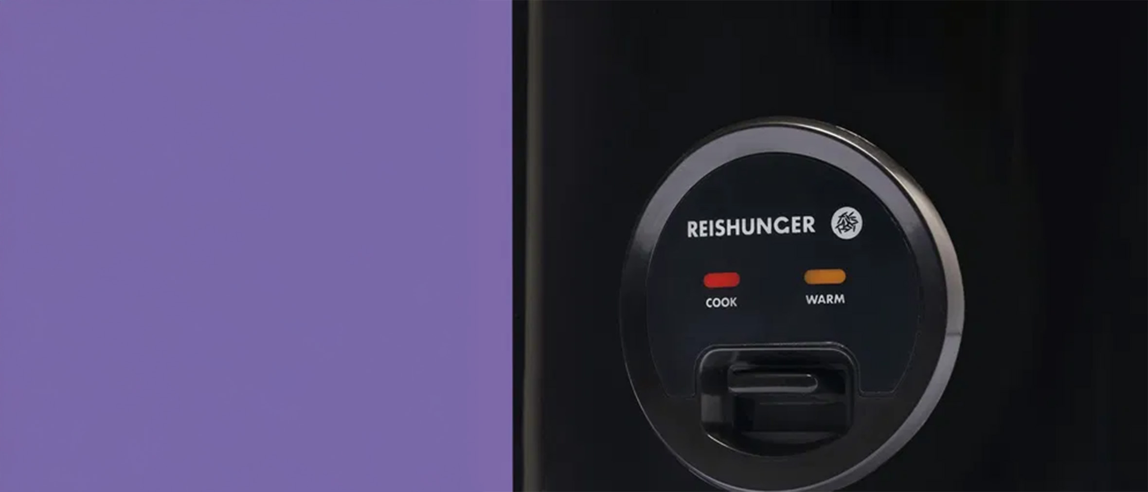 Ein schwarzes Gerät mit dem Namen "Reishunger". Auf dem Bedienfeld befinden sich zwei Lämpchen: ein rotes Licht für "Cook" (kochen) und ein orangefarbenes Licht für "Warm" (wärmen). Die Aufschrift ist klar und deutlich.