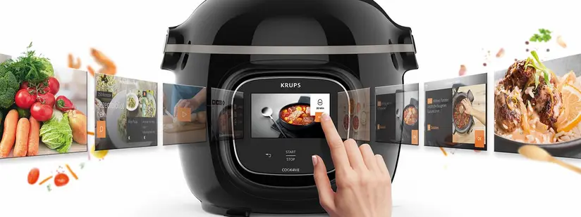 Das Bild zeigt einen modernen Kochautomaten von Krups mit einem digitalen Display. Eine Hand wählt Optionen auf dem Bildschirm aus, während Bilder von frischen Zutaten und fertigen Gerichten eingeblendet werden, die die Vielseitigkeit und Benutzerfreundlichkeit des Geräts hervorheben.