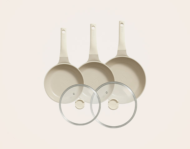 Drei beige Pfannen mit langen Griffen sind angeordnet, zwei kleinere Pfannen stehen seitlich und eine größere in der Mitte. Dazu gehören zwei durchsichtige Glasdeckel, die auf den Pfannen platziert werden können.