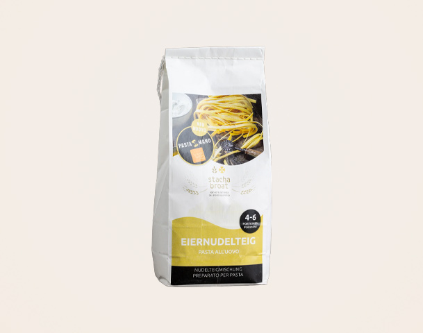 Eine weiße Verpackung für Eiernudelteig, beschriftet mit „EIERNUDELTEIG“ und „Pasta all’uovo“. Auf der Vorderseite sind Tipps und Informationen zur Verwendung des Teigs abgebildet. Die Verpackung ist für die Zubereitung von frischen Nudeln vorgesehen.