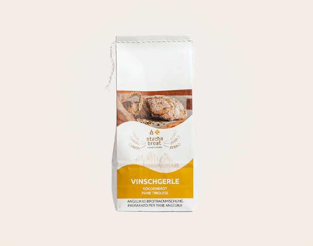 Eine Tüte mit Vinschgerle, einem traditionellen Roggenbrot. Das Design zeigt eine Abbildung des Brotlaibs und enthält den Hinweis auf die Backanleitung. Die Packung hat eine weiße Farbe mit einem gelben unteren Teil und Schriftzügen in verschiedenen Farben.