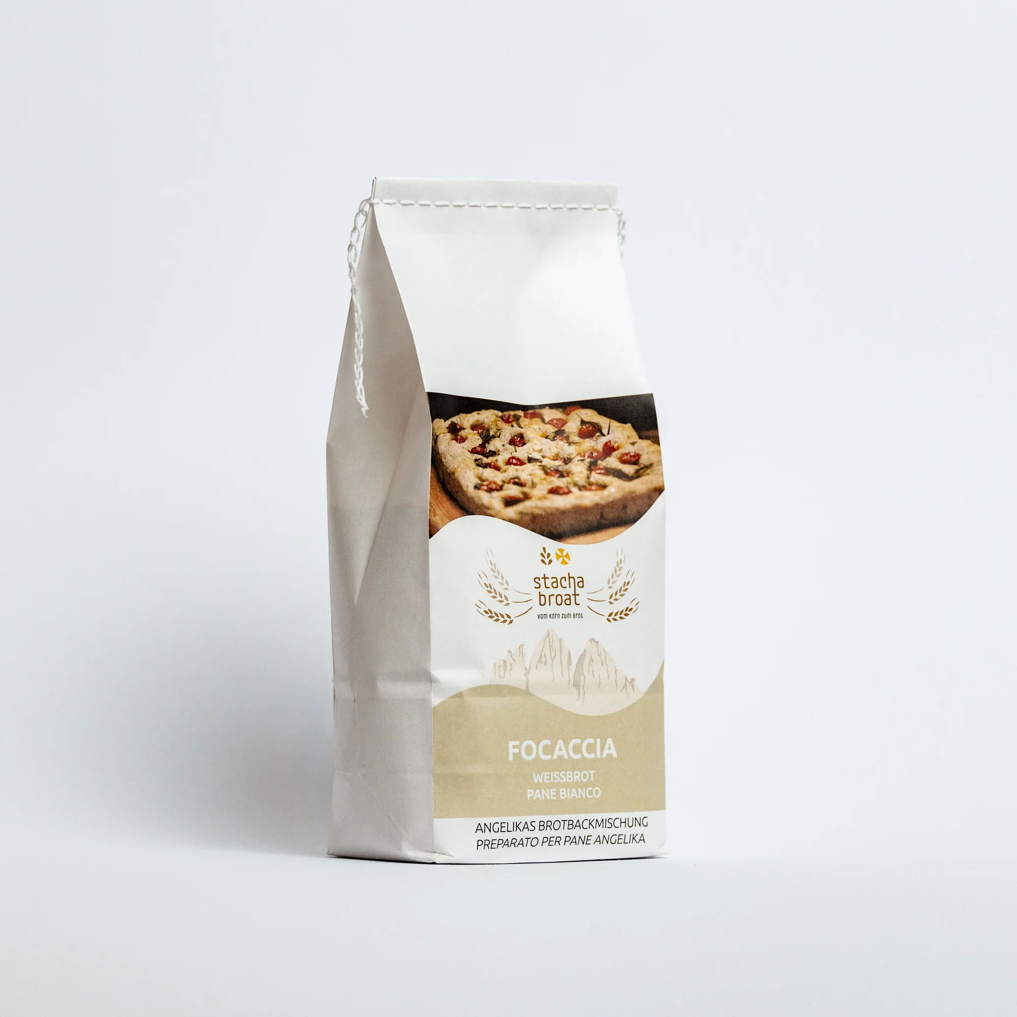 Eine weiße Papiertüte mit dem Aufdruck "Focaccia" in verschiedenen Sprachen, darunter Deutsch und Italienisch. Auf der Vorderseite ist ein Bild von einer belegten Focaccia abgebildet. Die Tüte enthält eine Brotmischung von "Stach Broat".