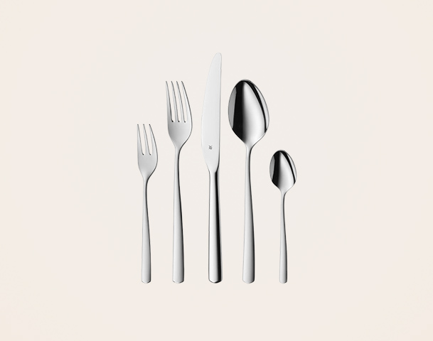 Eine Anordnung von fünf Besteckteilen auf hellem Hintergrund: ein Esslöffel, eine Gabel, ein Messer, eine kleine Gabel und ein kleiner Löffel. Alle Bestecke sind aus Edelstahl und haben ein schlichtes, modernes Design.
