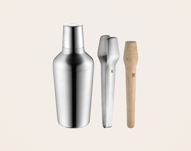 Ein Set aus einem eleganten, silbernen Cocktailshaker, einer silbernen Zange und einem hölzernen Muddler. Diese Utensilien sind für die Zubereitung von Cocktails und Drinks konzipiert.