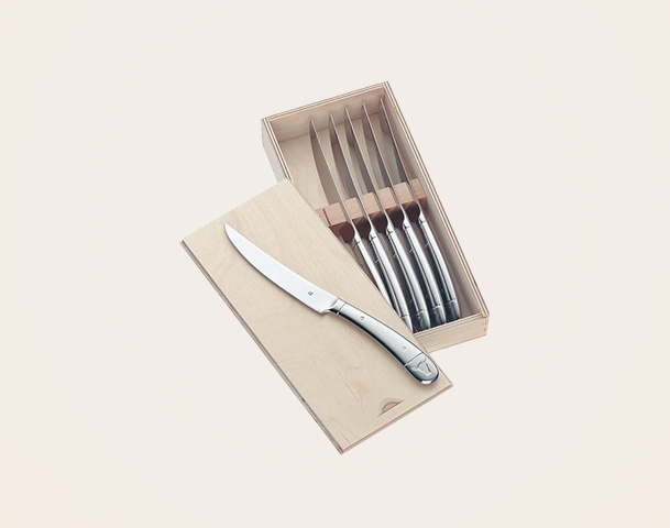 Eine Holzbox mit mehreren Besteckmessern. Ein Messer liegt offen neben der Box, während die anderen fünf in der Box aufbewahrt sind. Die Klingen sind aus Edelstahl, und die Griffe sind schlicht gestaltet.