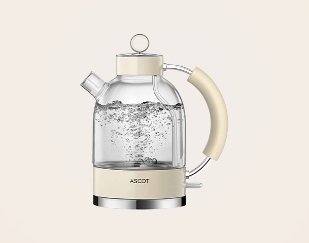 Ein transparenter Wasserkocher mit einer beige-farbenen Griffe, der Wasser kocht. Die Blasen im kochenden Wasser sind sichtbar. Der Kessel hat eine runde Form mit einem klaren Deckel und einem Ausguss. Die Marke „ASCOT“ ist am unteren Teil des Geräts zu sehen.