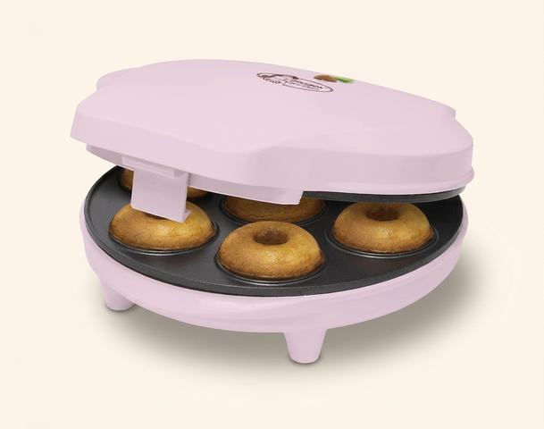 Ein rosa Donut-Maker mit geöffnetem Deckel, der fünf frisch gebackene Donuts zeigt. Die Donuts sind goldbraun und formenrund. Der Gerät hat eine einfache, kompakte Form und steht auf kleinen Füßen.