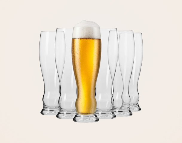 Ein gefülltes Glas mit goldenem Bier und einer Schaumkrone steht in der Mitte vor mehreren leeren Gläsern. Die Gläser sind in einer symmetrischen Anordnung angeordnet. Der Hintergrund ist einfarbig.