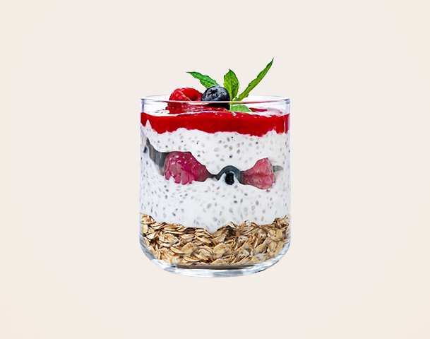 Ein Glas mit Schichten aus Haferflocken, Joghurt, Himbeeren und Heidelbeeren, bedeckt mit einer roten Fruchtsoße und garniert mit einem Minzblatt. Das Dessert hat eine ansprechende Präsentation durch die verschiedenen Farbschichten.
