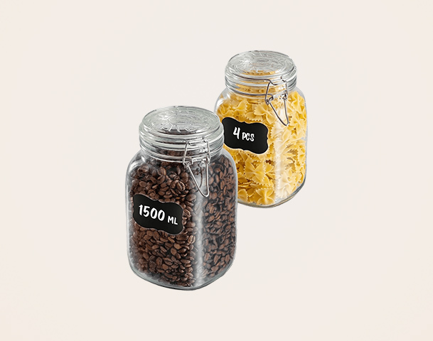 Zwei Glasbehälter stehen auf einem hellen Hintergrund. Der linke Behälter enthält Kaffeebohnen und hat eine Beschriftung von 1500 ml. Der rechte Behälter enthält Nudeln und ist mit "4 Stück" beschriftet. Neben den Behältern liegen ein paar Etiketten.
