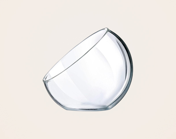Eine transparente, bauchige Glasschüssel steht schräg auf einer hellen Fläche. Sie hat eine glatte Oberfläche und einen leicht gewölbten Boden, der sie einzigartig macht.