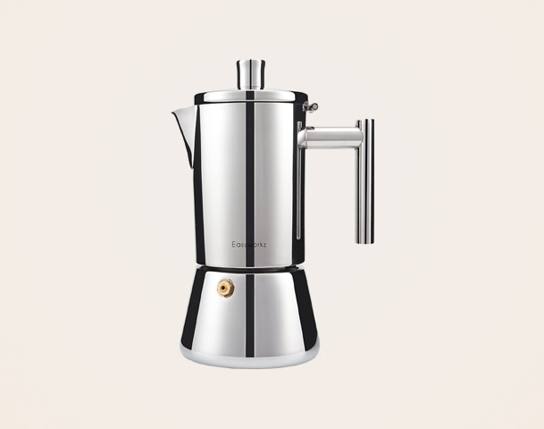 Eine glänzende, silberne Espressokanne aus Edelstahl steht auf einem hellen Hintergrund. Sie hat einen runden Boden, einen schmalen Körper und einen Ausguss mit einem abnehmbaren Deckel. Der Griff ist gut sichtbar und sorgt für eine ergonomische Handhabung.