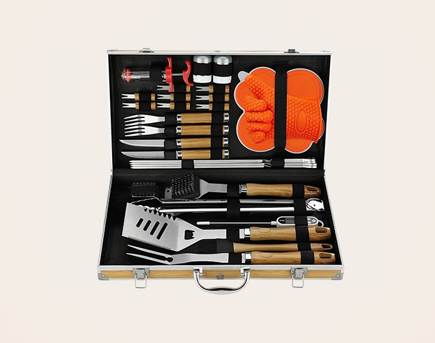 Das Bild zeigt einen offenen Grillwerkzeugkoffer, der verschiedene Utensilien enthält, darunter Grillzangen, Wender, Gabeln, Pinsel und Grillhandschuhe. Die Werkzeuge haben Holzgriffe und sind ordentlich im Koffer angeordnet, der eine stylische, schwarze Innenausstattung hat.