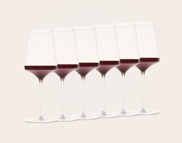 Sechs Weingläser stehen in einer Reihe, gefüllt mit rotem Wein. Die Gläser sind elegant mit langen Stielen und widerstrahlen das Licht. Der Hintergrund ist neutral und unauffällig, sodass die Gläser im Fokus stehen.