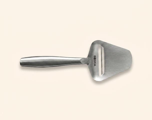 Ein schmaler, metallischer Käsehobel mit einem breiten, flachen Ende und einem langen Griff. Die Klinge ist an einer Seite gezackt, um Käse in Scheiben zu schneiden. Das Logo "BOSKA" ist auf der Vorderseite des Griffs sichtbar.