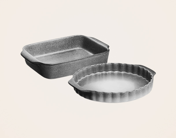 Zwei Backformen sind abgebildet: eine rechteckige, flache Form und eine runde Form mit gewelltem Rand. Beide Formen sind aus einem dunklen, matten Material und ideal zum Backen von Aufläufen oder Torten geeignet.