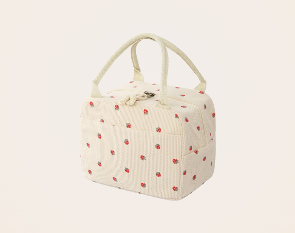 Eine hellbeige Tasche mit einem dichten, strukturierten Stoff, verziert mit roten Punkten. Sie hat zwei Tragegriffe und eine quadratische Form. Die Tasche eignet sich gut für den Transport von Lebensmitteln oder anderen Kleinigkeiten.