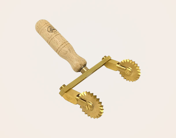 Ein goldenes Teigschneider-Werkzeug mit einem Holzgriff. Es verfügt über zwei radialen, gezackten Räder, die zum Schneiden von Teig oder zum Dekorieren von Oberflächen verwendet werden können.