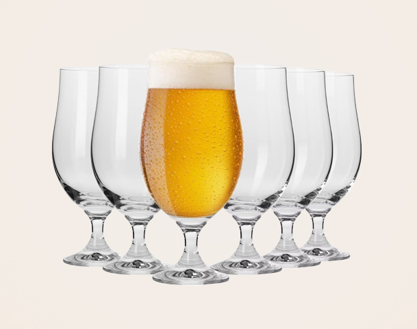Ein vollgefülltes, schäumendes Bierglas steht in der Mitte vor mehreren leeren Gläsern. Die Gläser sind klar und glänzend, während das Bier eine goldene Farbe hat und von Wassertropfen bedeckt ist.