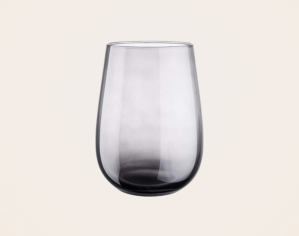 Ein transparentes, leicht oval geformtes Glas mit einem grauen Schimmer. Es steht auf einem hellen Hintergrund und hat keine zusätzlichen Elemente oder Dekorationen.