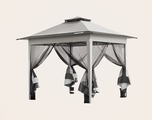 Ein moderner Pavillon mit schrägem Dach und vier Seiteneingängen, die von halbtransparenten Vorhängen umgeben sind. Die Vorhänge sind grau und schwarz und hängen locker an den Seiten. Der Pavillon bietet Schutz vor Sonne und leichten Regen.