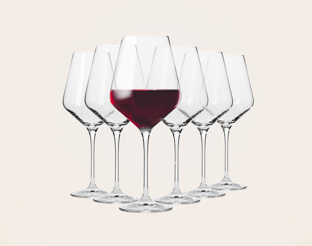 Sechs Weingläser stehen in einer Reihe auf einem hellen Hintergrund. In der Mitte hebt sich ein Glas mit rotem Wein hervor, während die anderen Gläser leer sind.
